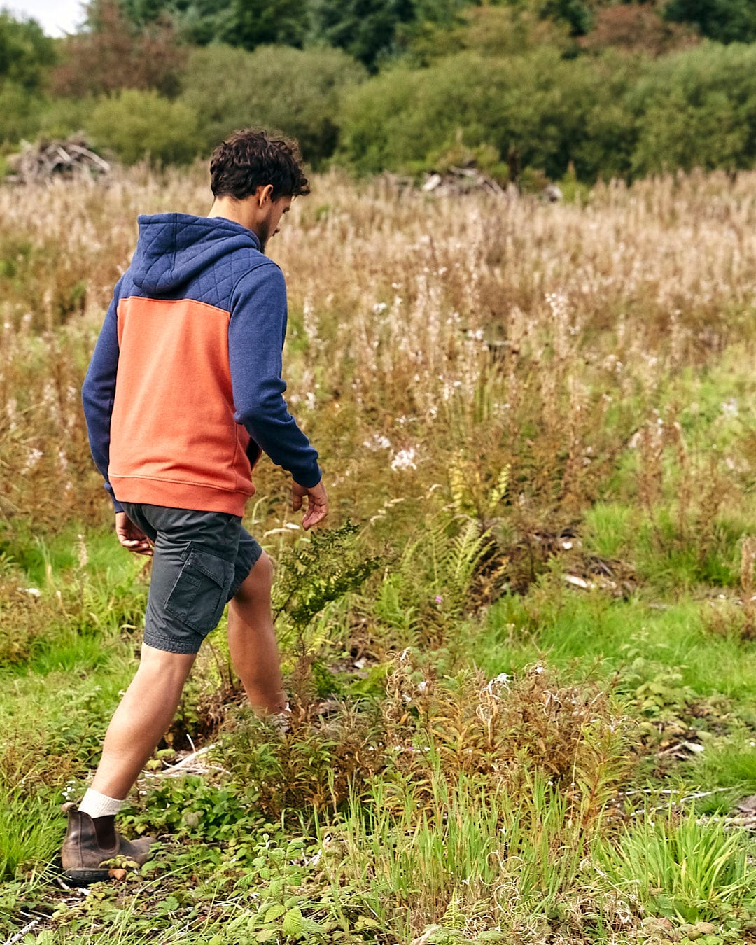 A man walking through a grassy field in an Aiken - Mens 1/4 Neck Hoodie - Orange by Saltrock.