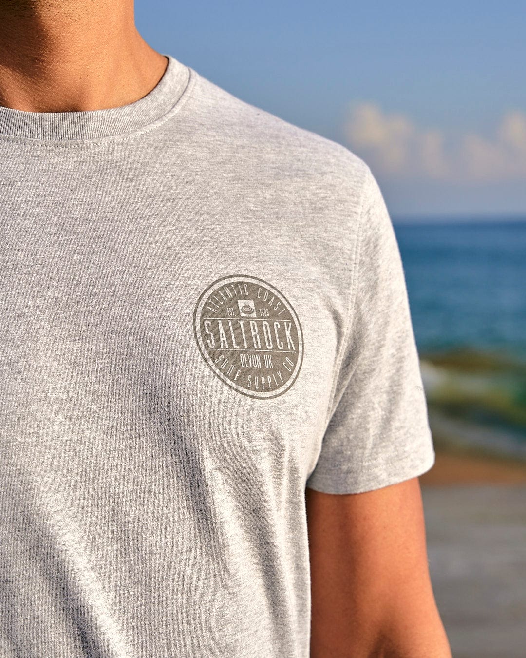 A man wearing the Saltrock All Terrain - Mens Short Sleeve T-Shirt - Grey on the beach.