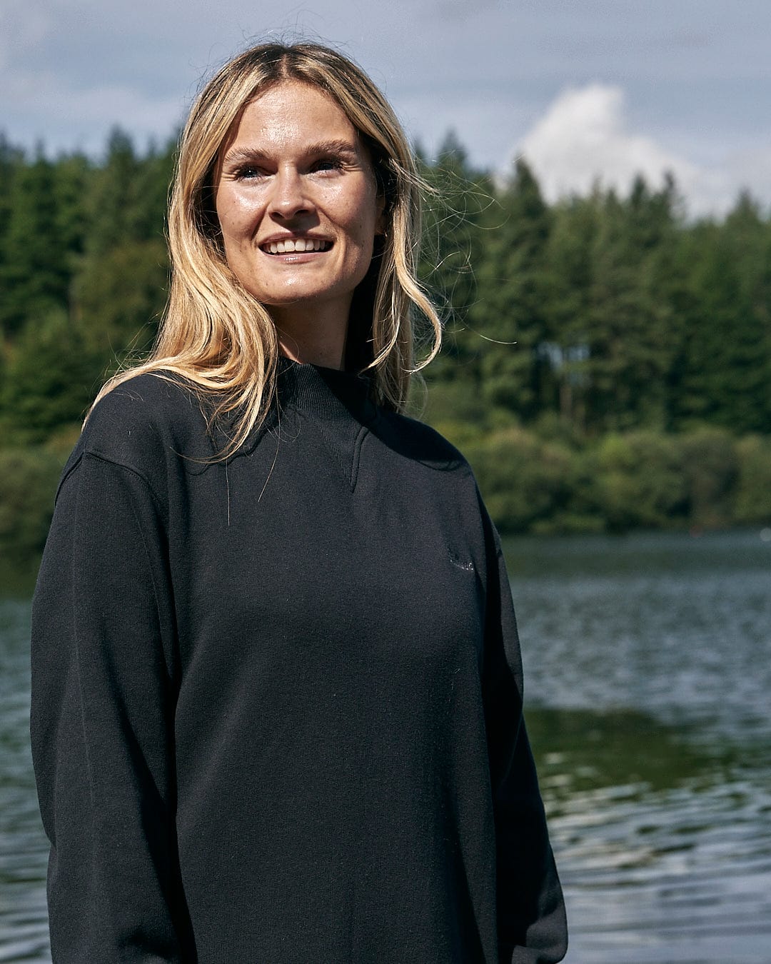 A woman standing in front of a lake wearing a Saltrock Alma - Womens Balloon Sleeve Sweat Dress - Black.