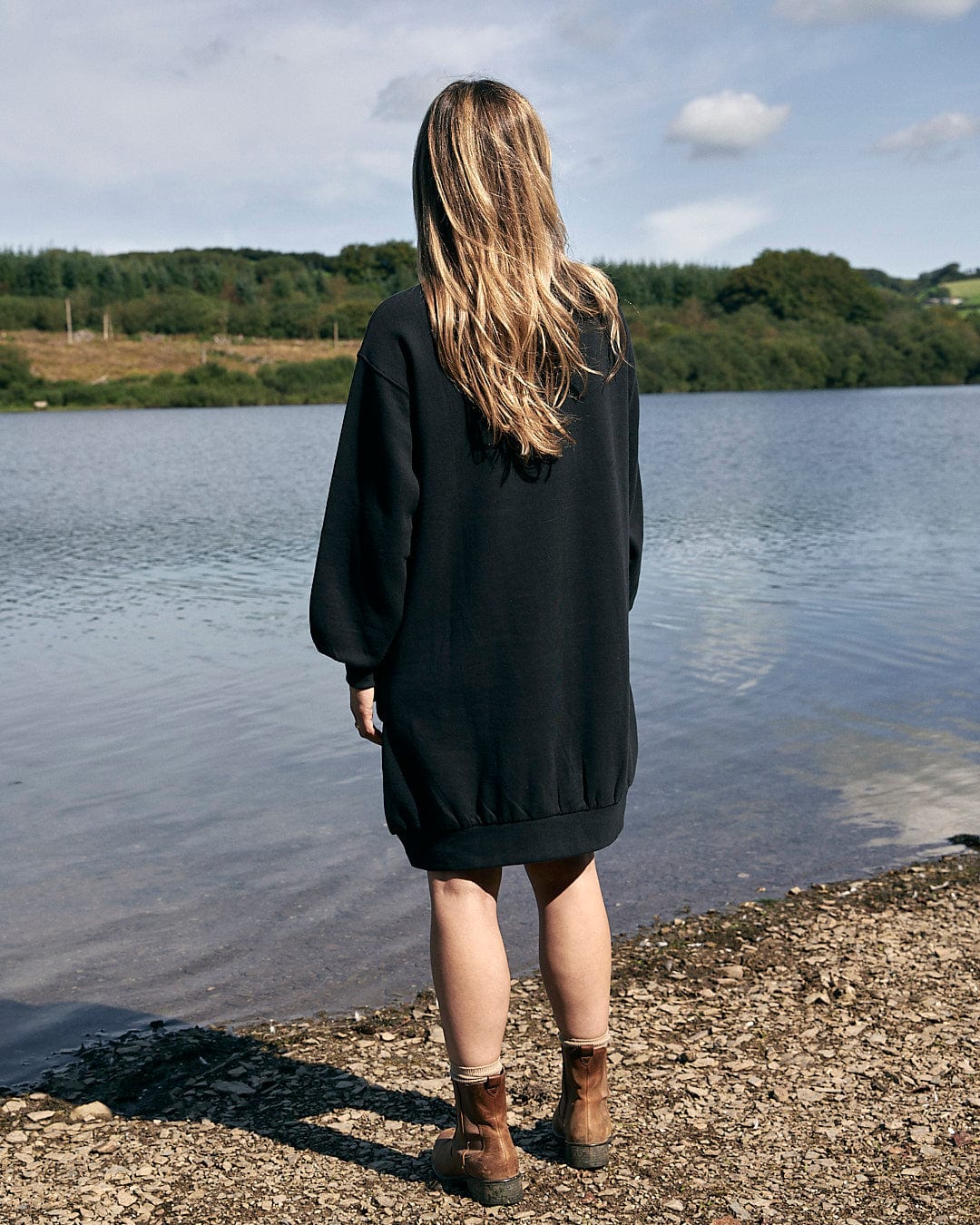 A woman standing by a lake in a Saltrock Alma - Womens Balloon Sleeve Sweat Dress - Black.