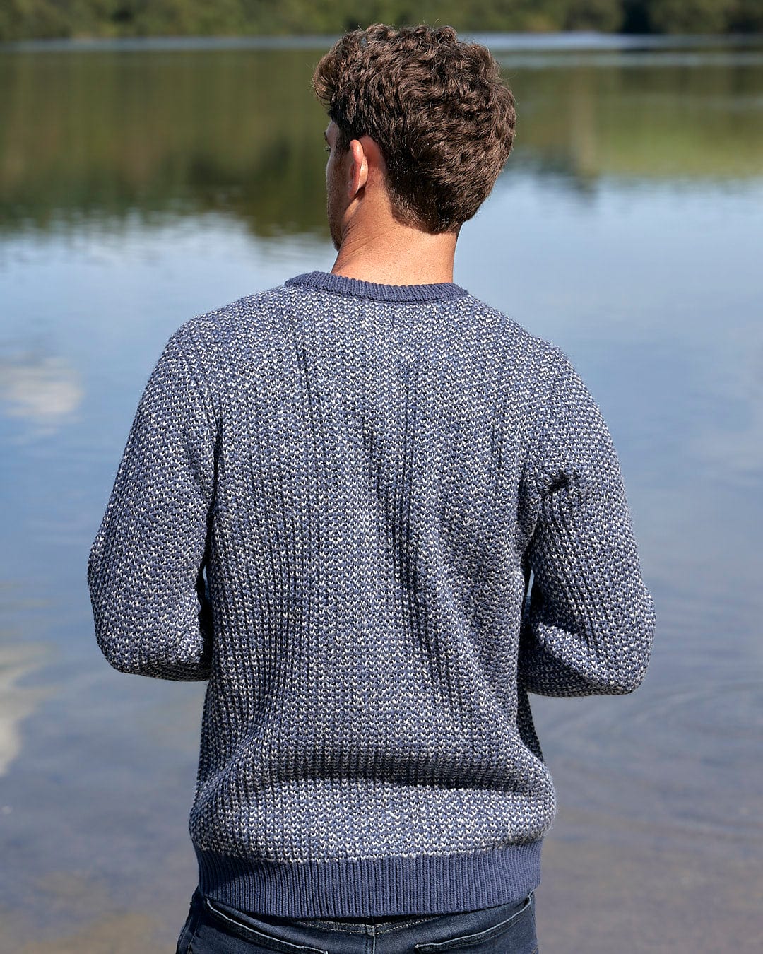 A man is standing by a body of water wearing a Saltrock Arlen - Mens Crew Knit - Dark Blue sweater.