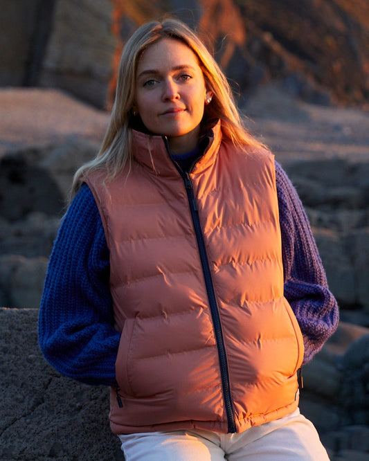 A woman wearing an Astra - Womens Reversible Padded Gilet - Blue/Pink jacket with a detachable hood from Saltrock.
