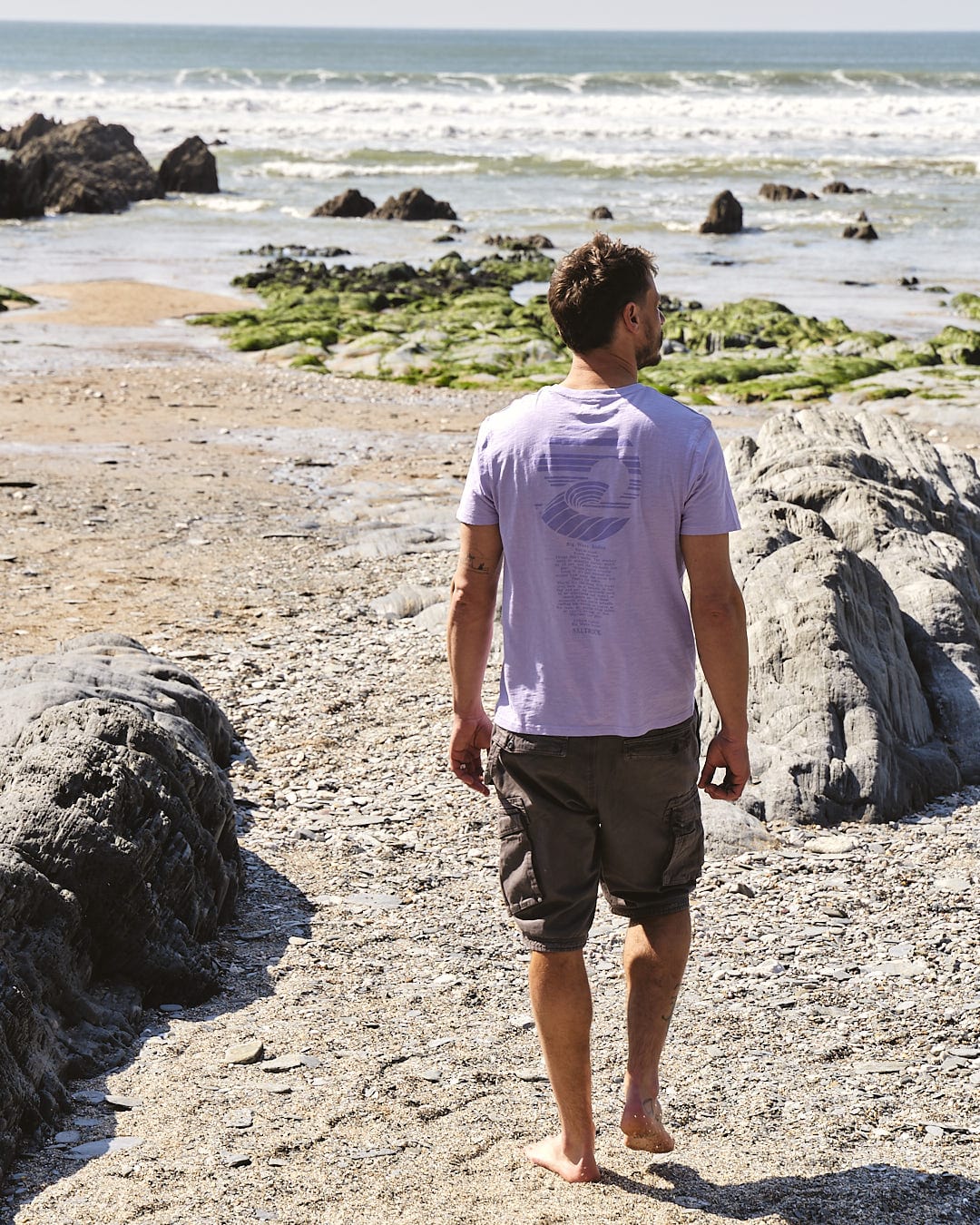 A man walking on the beach with a Saltrock Atlantic - Mens Short Sleeve T-Shirt - Purple.