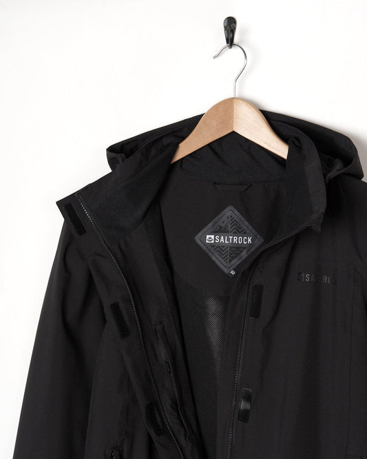 A black waterproof Saltrock Aubrey jacket hanging on a wooden hanger against a white background, showing the front view with zippers and hood.
