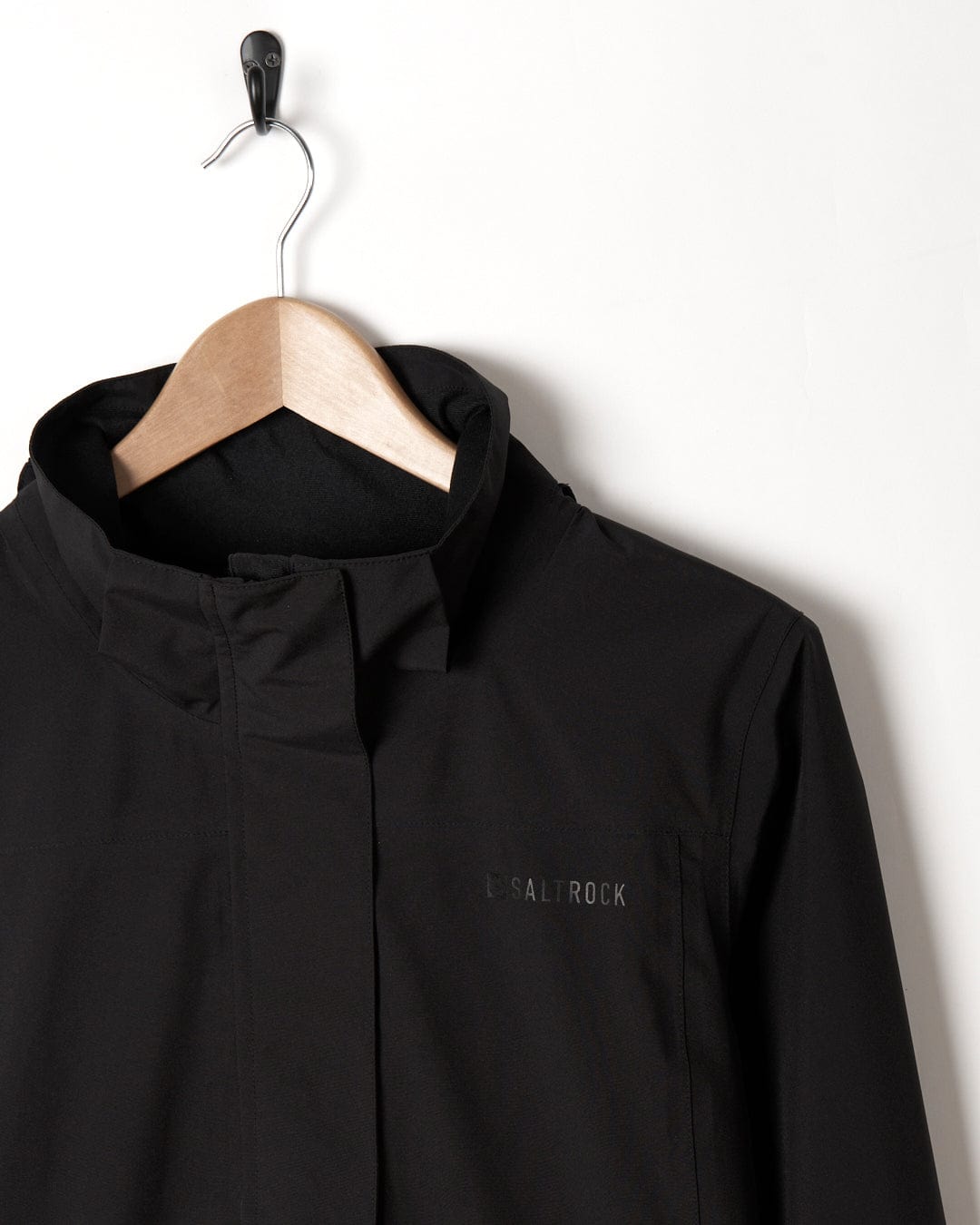 Aubrey - Womens Waterproof Jacket - Black by Saltrock hanging on a wooden hanger against a white background, with the brand "Saltrock" embroidered on the left side.