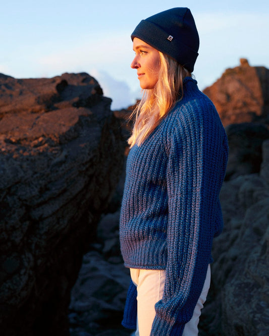 A woman wearing a Mandy - Saltrock Womens Funnel Neck Jumper - Blue, also known as a blue jumper, and a beanie.