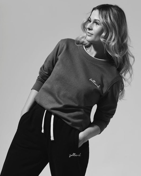 A woman donning a Saltrock branded Velator - Long Sleeve Sweatshirt - Khaki, made with soft material, paired with comfortable black sweatpants.
