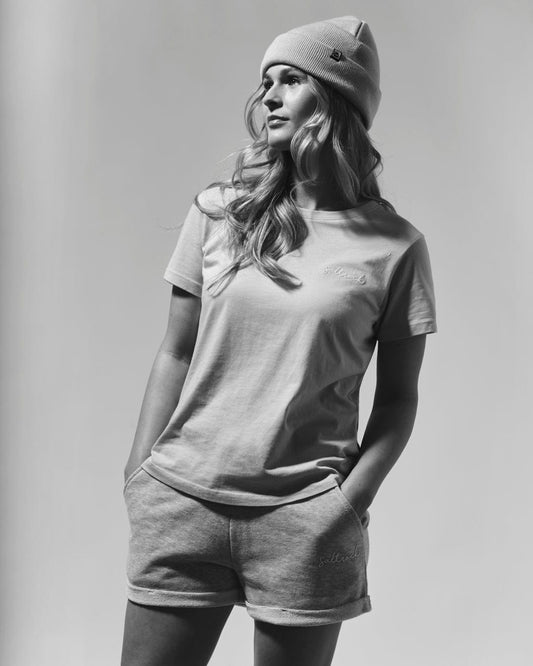 A woman in a casual outfit consisting of a Saltrock Velator Women's Short Sleeve T-Shirt in Grey Marl with a crew neckline and shorts, wearing a beanie, poses in a grayscale photo.