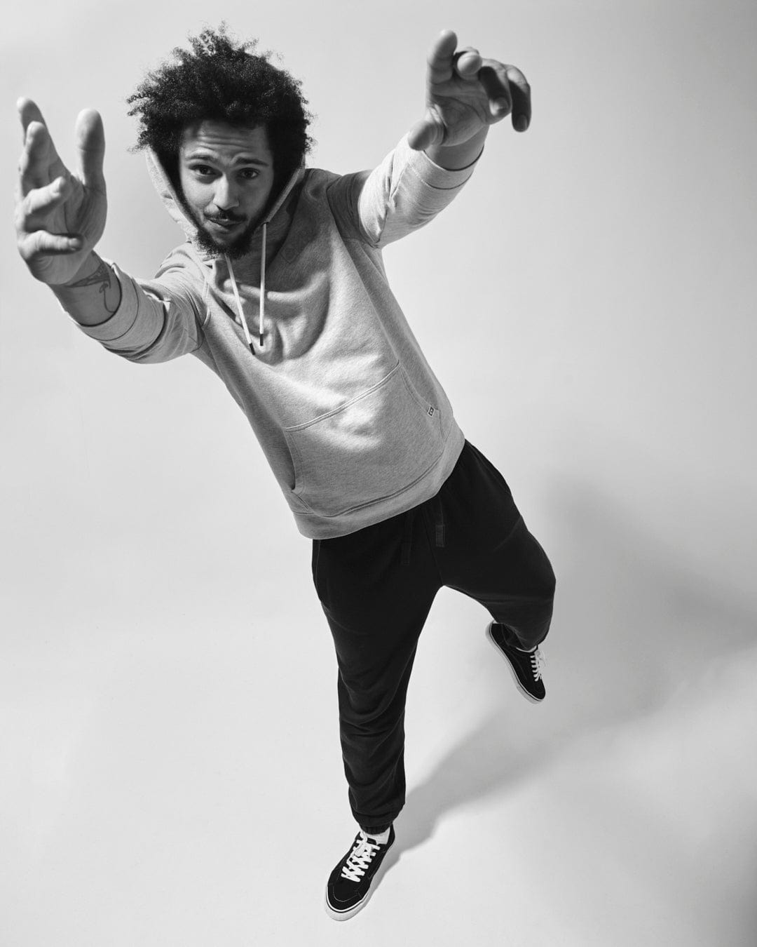 A black and white photo of a person in mid-jump, wearing a Saltrock Original - Mens Pop Hood - Blue Marl hoodie and sneakers made from soft jersey material, extending arms towards the camera with fingers pointed.