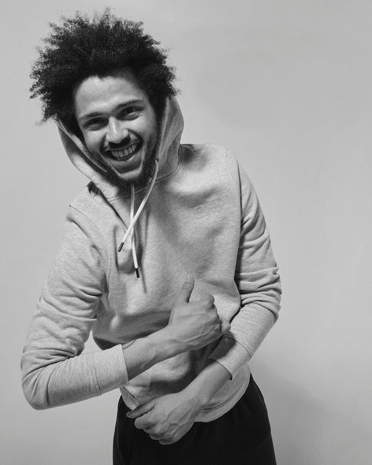 A person with a cheerful expression, wearing a Saltrock Original - Mens Pop Hoodie in Grey made of jersey material, is seen laughing and clutching their stomach as if in a moment of genuine amusement or joy. The image is black and white.
