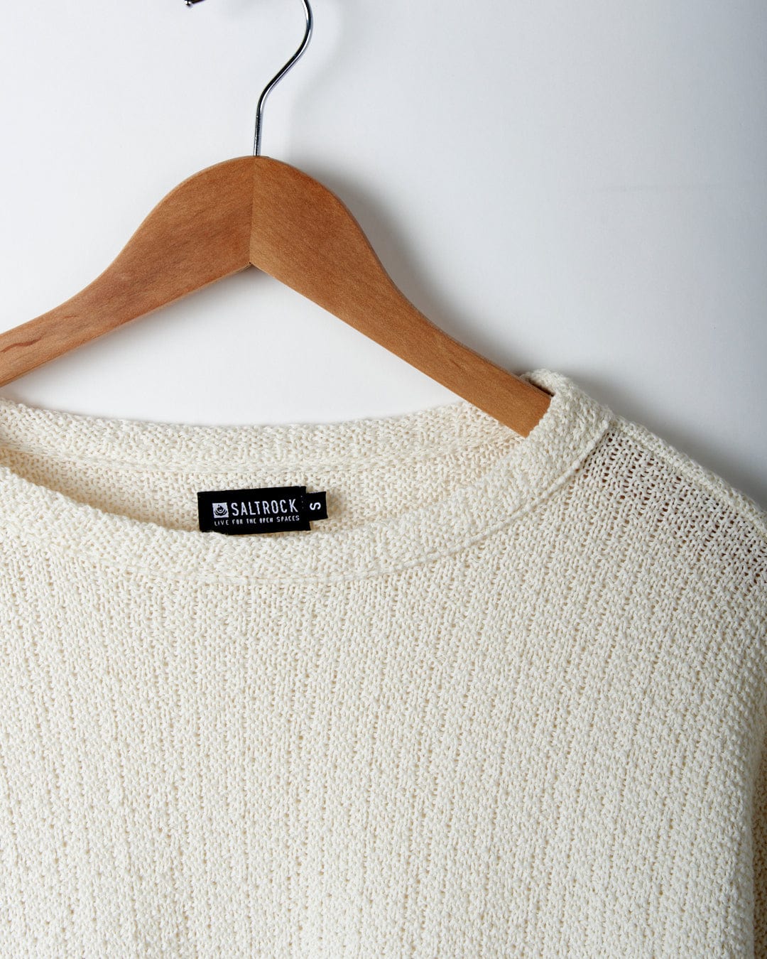 Beige textured knit sweater on a wooden hanger against a white background, with a visible brand label that reads 