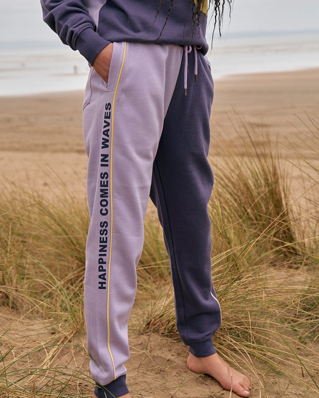 A woman standing on the beach wearing a Saltrock sweatshirt and Saltrock sweatpants, Betty - Womens Jogger - Light Purple.