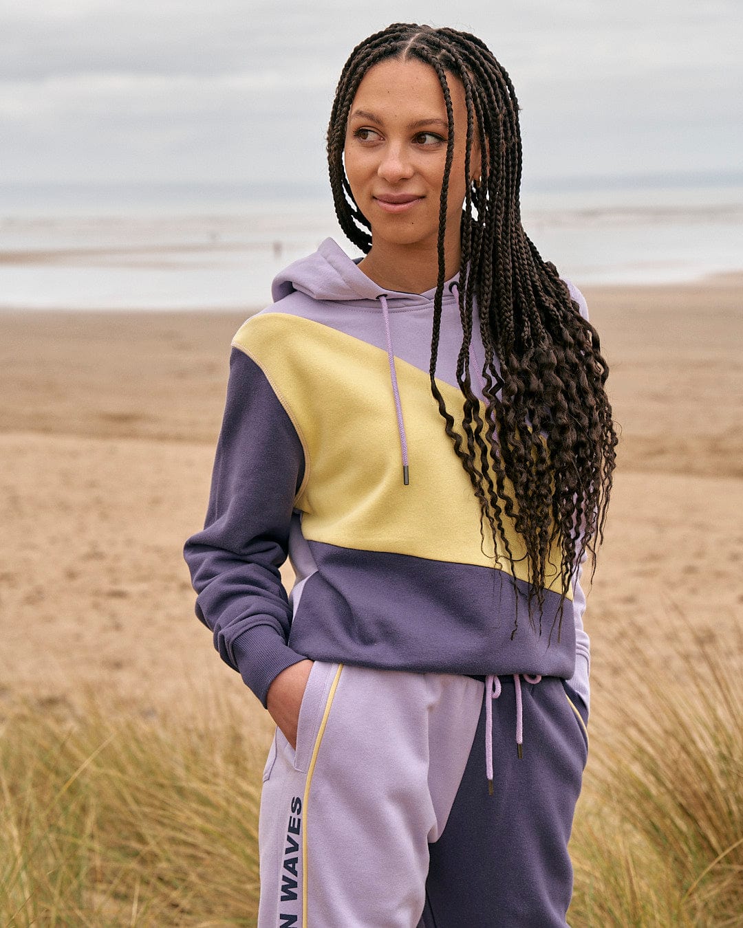 A woman in a Saltrock Betty - Womens Jogger - Light Purple hoodie standing on the beach.