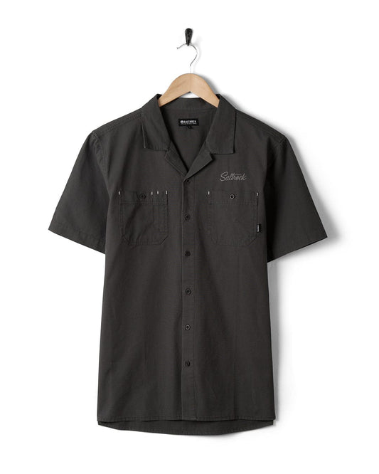 A black short sleeve Boulevard - Mens Short Utility Sleeve Shirt - Dark Grey featuring Saltrock branding, hanging on a hanger.