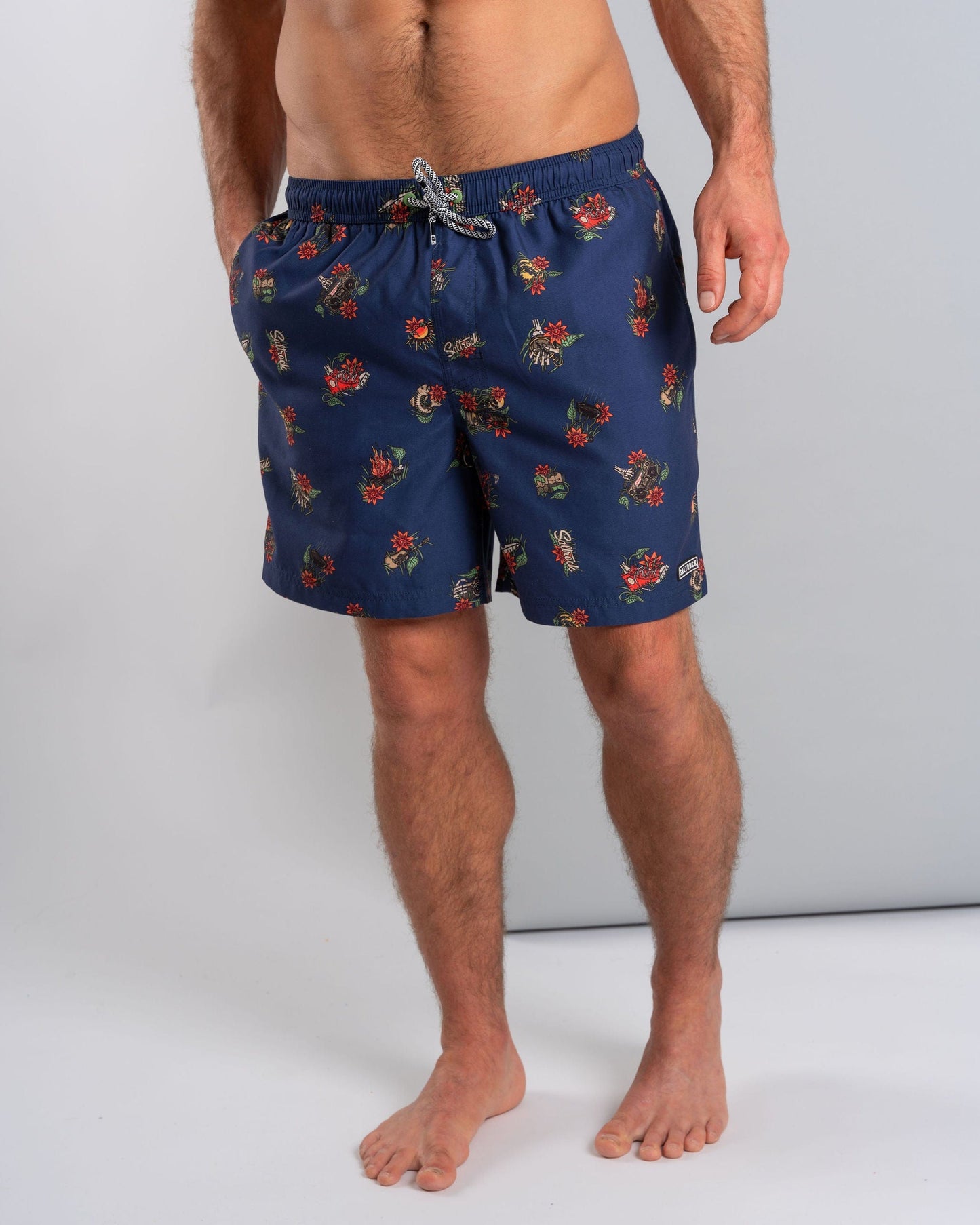 A man stands barefoot against a plain background wearing Saltrock's Wanderer swim shorts in blue, featuring a floral print and an elasticated waist.