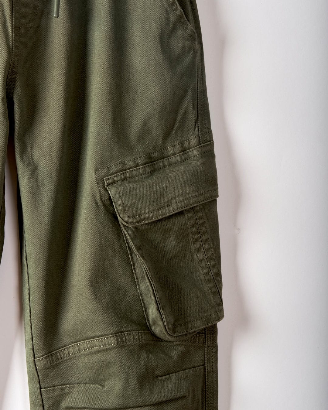 Close-up of Saltrock's Bora Bora Kids Chino Trousers in dark green, featuring a large flap cargo pocket and an elasticated waist, shown against a plain white background.