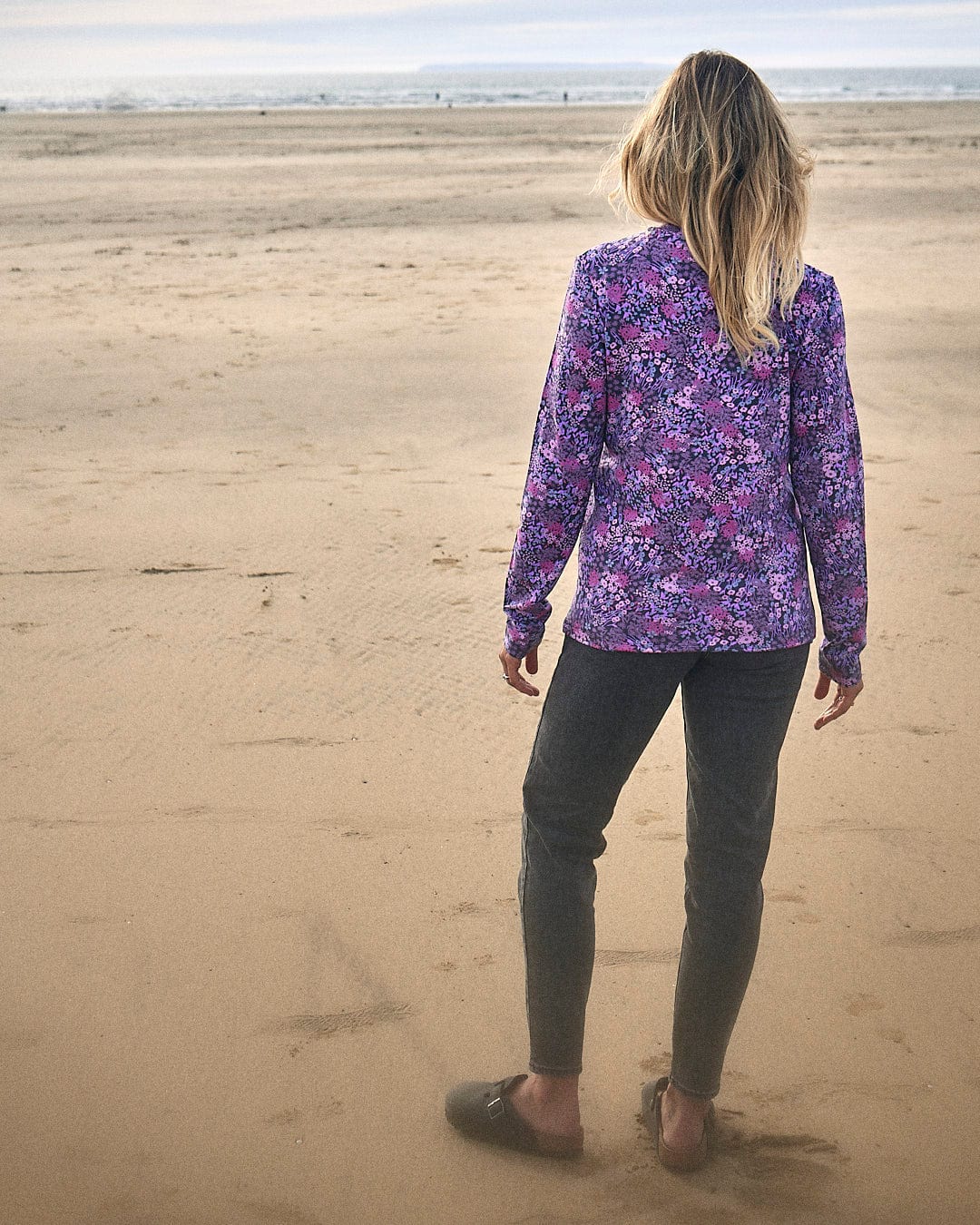 A woman standing on a beach wearing a Saltrock Brooklyn - Womens Long Sleeve T-Shirt - Purple made of jersey material.