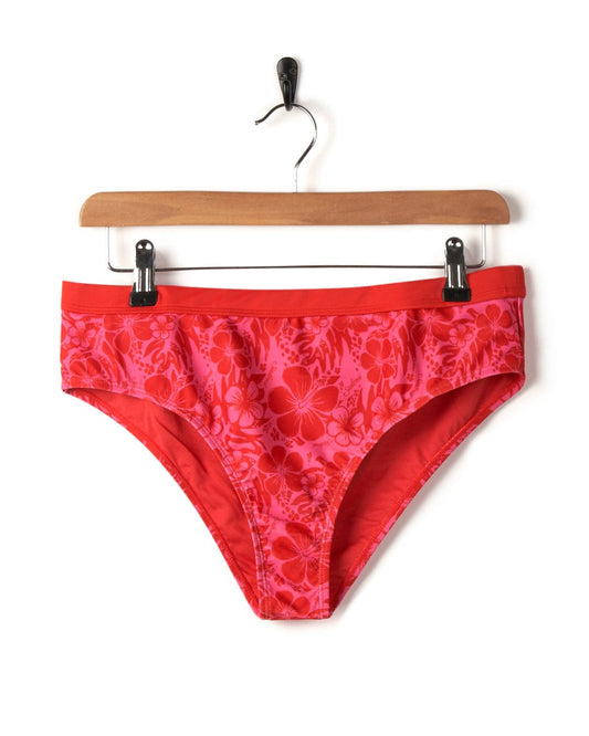 Red Caeley - Recycled Womens Hibiscus Bikini Bottoms - Pink underwear hanging on a wooden hanger against a white background.