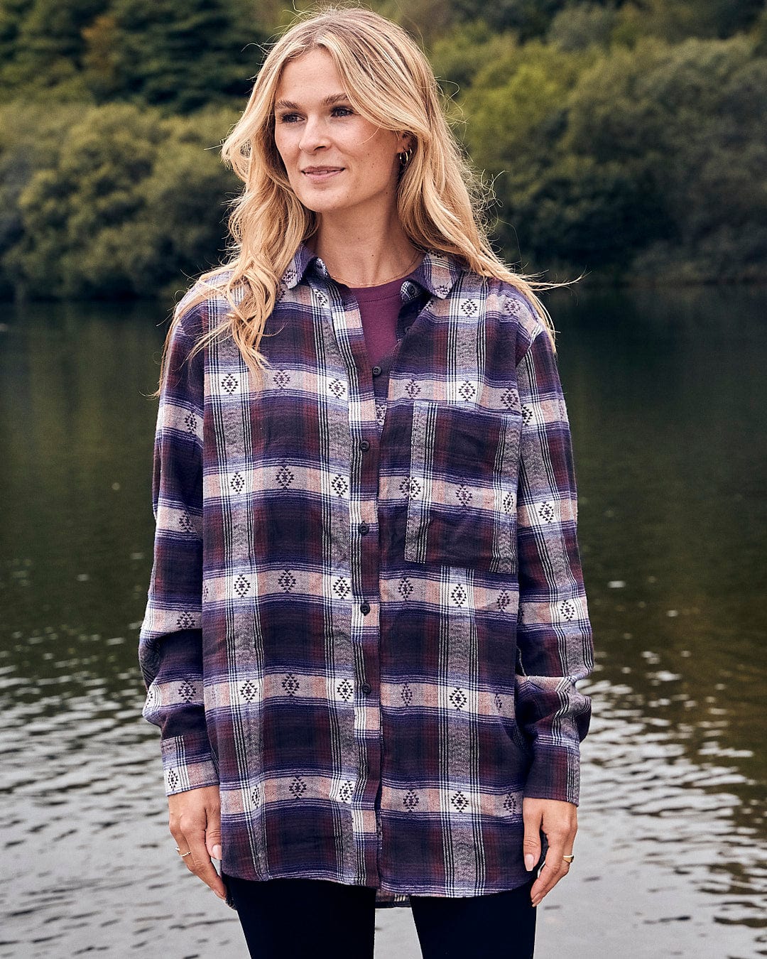 A woman wearing a Saltrock Camille - Womens Jaquard Check Boyfriend Shirt - Purple standing by a lake.