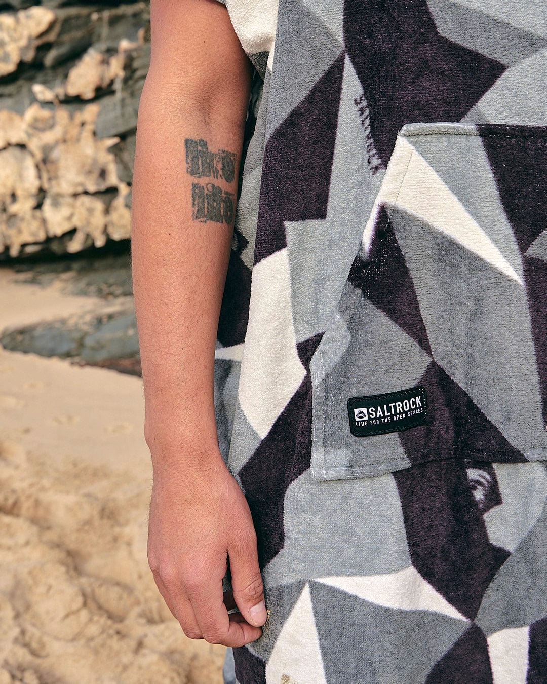 A person wearing a Saltrock Geo Camo - Changing Towel - Grey hoodie on the beach.