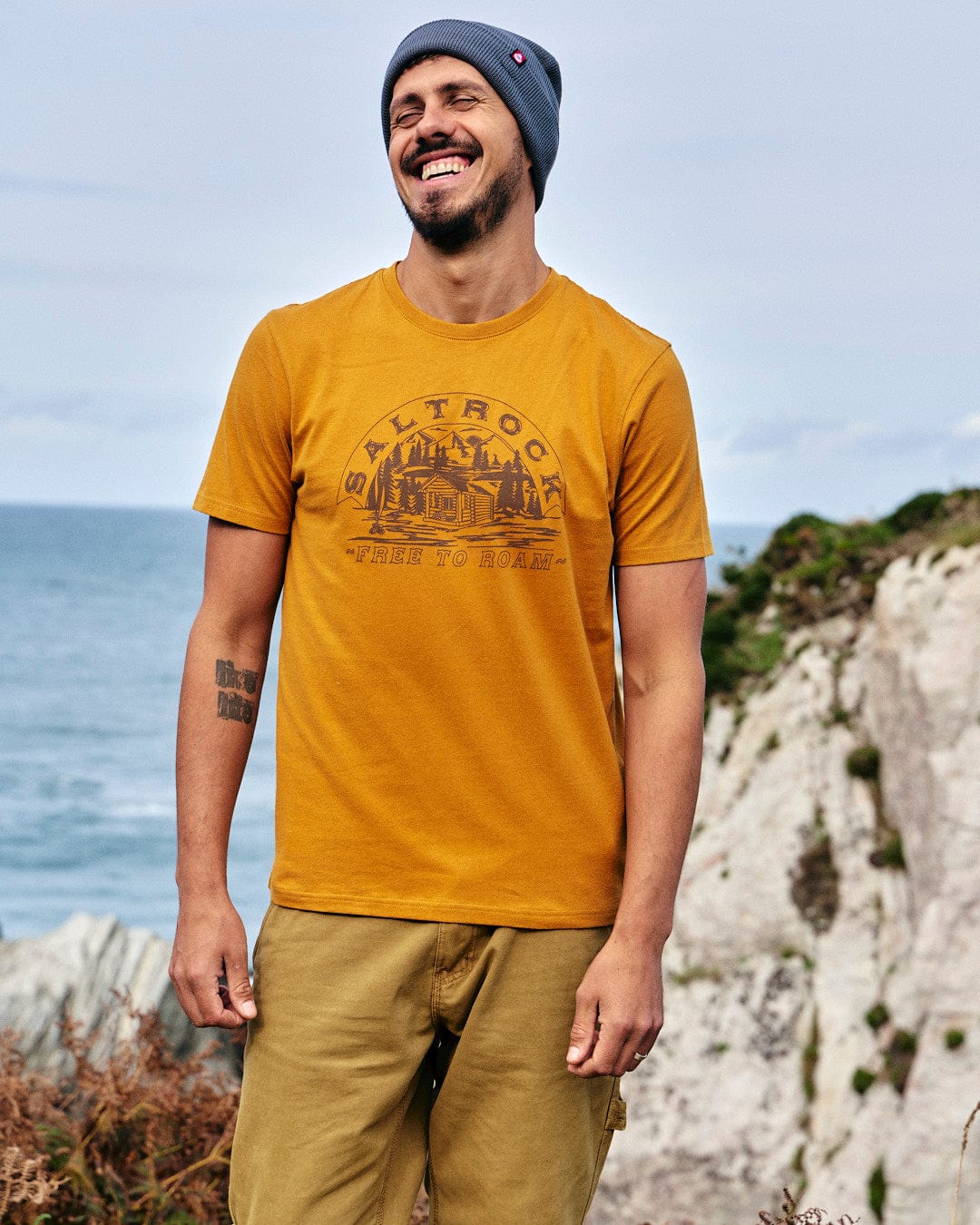 A man wearing a yellow Saltrock Camping Cabin - Mens Short Sleeve T-Shirt and khaki pants.