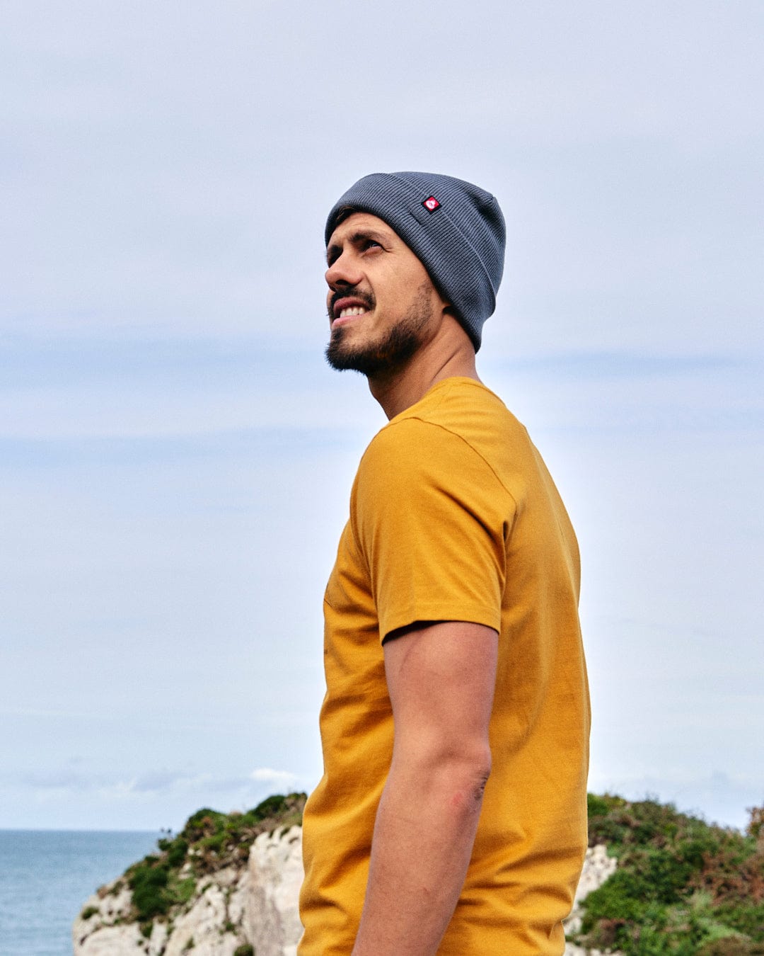 A man wearing a yellow Saltrock Camping Cabin - Mens Short Sleeve T-Shirt and beanie.