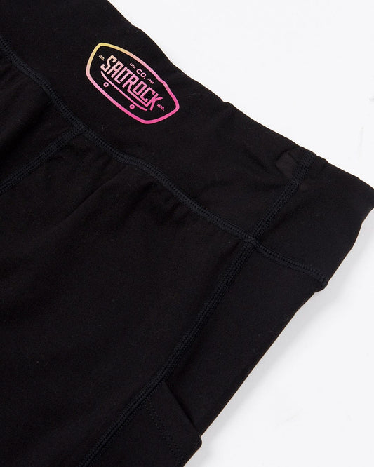 A Carly - Kids Cycling Short - Black with a pink logo on it, made from soft fabric by Saltrock.