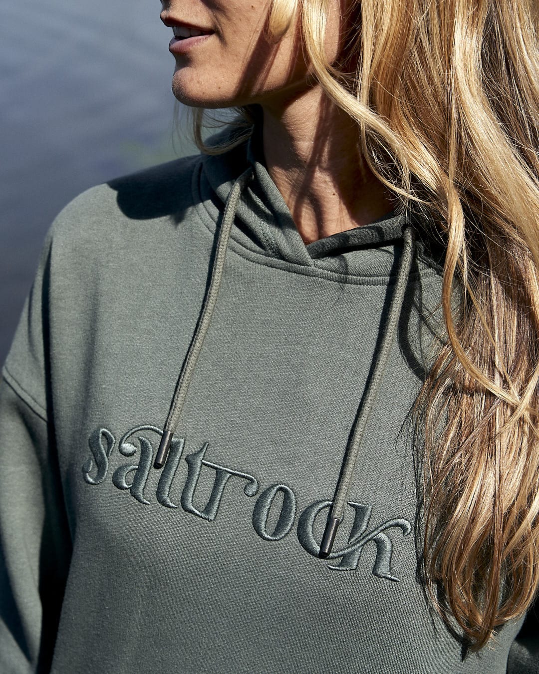 A woman wearing a Celeste - Womens Pop Hoodie - Dark Green with Saltrock branding and drawstring hood.