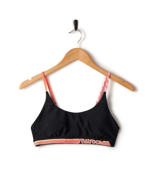 Cleo - Recycled Womens Retro Bikini Top - Black sports bra with orange trim and adjustable straps hanging on a wooden hanger against a white background. (Saltrock)