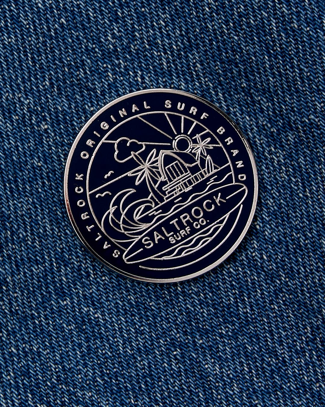 Round black and white Saltrock branded patch with silver graphics on navy denim fabric.