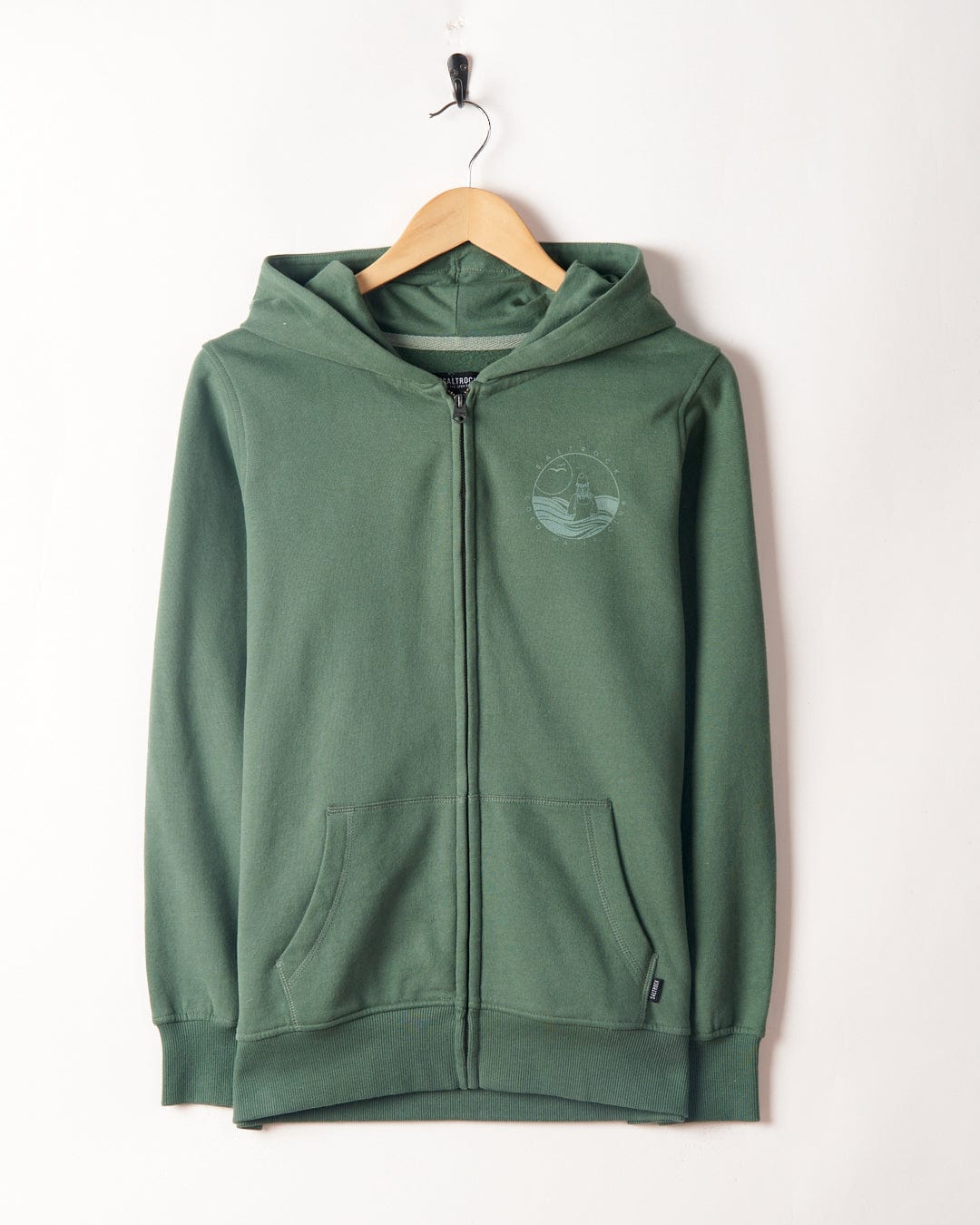 Saltrock Coldwater Club Ladies Zip Hoodie in Green with a peached soft hand feel and a logo on the left chest, hanging on a hook against a white wall.