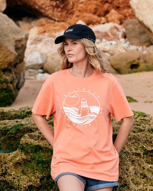 A woman wearing a Saltrock Coldwater Club Womens Short Sleeve T-Shirt in Peach standing on rocks.