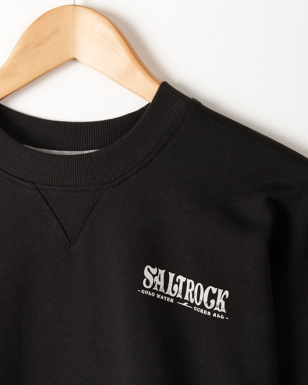 Black oversized T-shirt with "Saltrock - Cold Water - Mens Oversized Sweat - Black" logo, hanging on a wooden hanger against a white background.