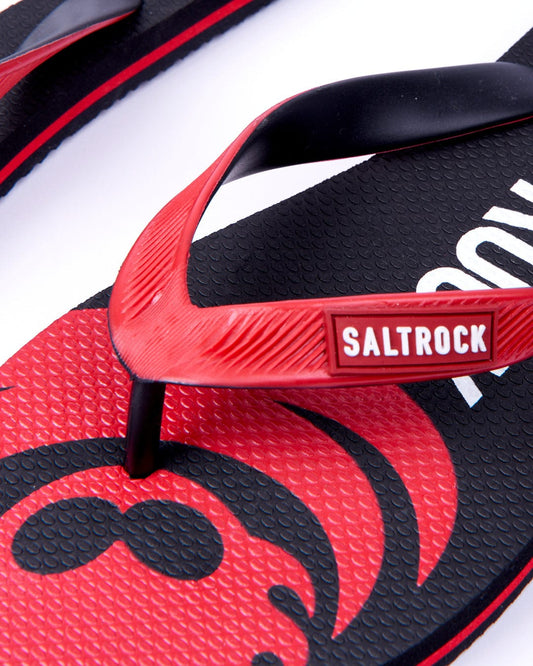 Close-up of a black and red Saltrock Corp Flame flip-flop with textured flamehead soles and logo detail.