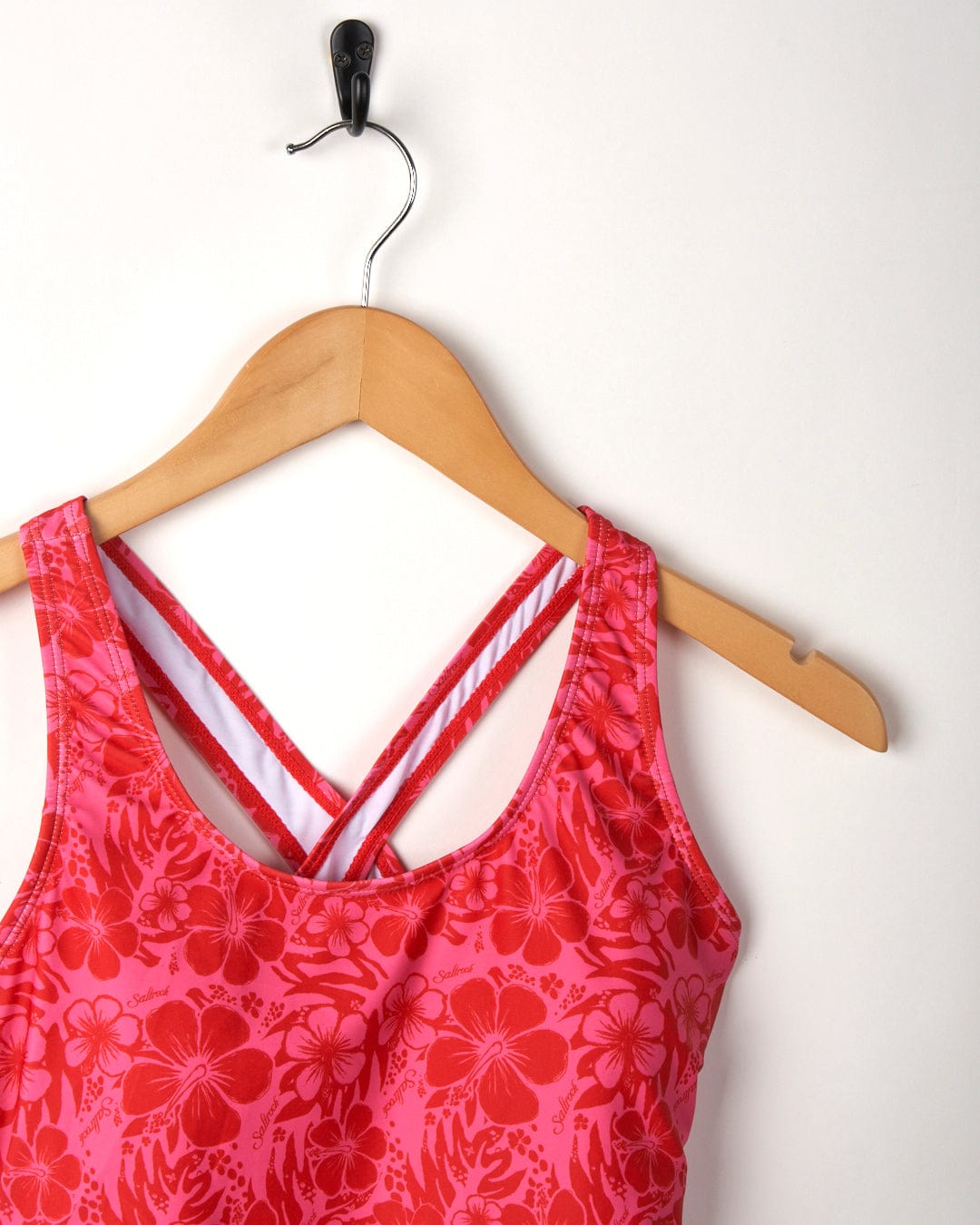 Corrine Hibiscus full piece swimsuit with crisscross straps hanging on a wooden hanger against a white background.