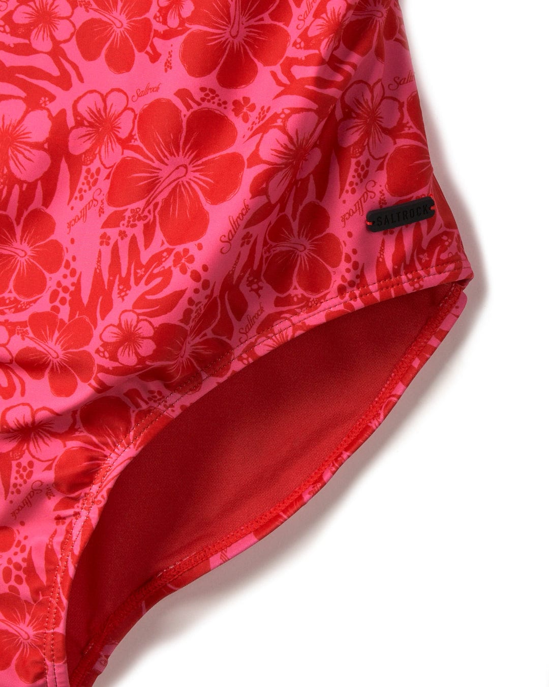 Close-up of a red Corrine Hibiscus - Recycled Womens Swimsuit - Pink with a visible brand tag reading "Saltrock.