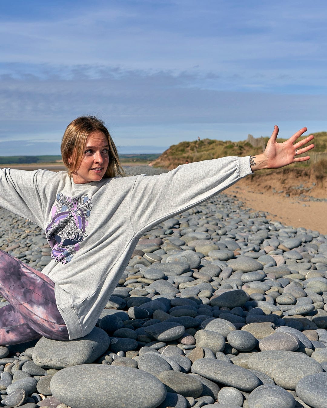 A woman embracing comfort in a Cosmic Soul Womens Longline Sweat - Light Grey by Saltrock on a longline beach.