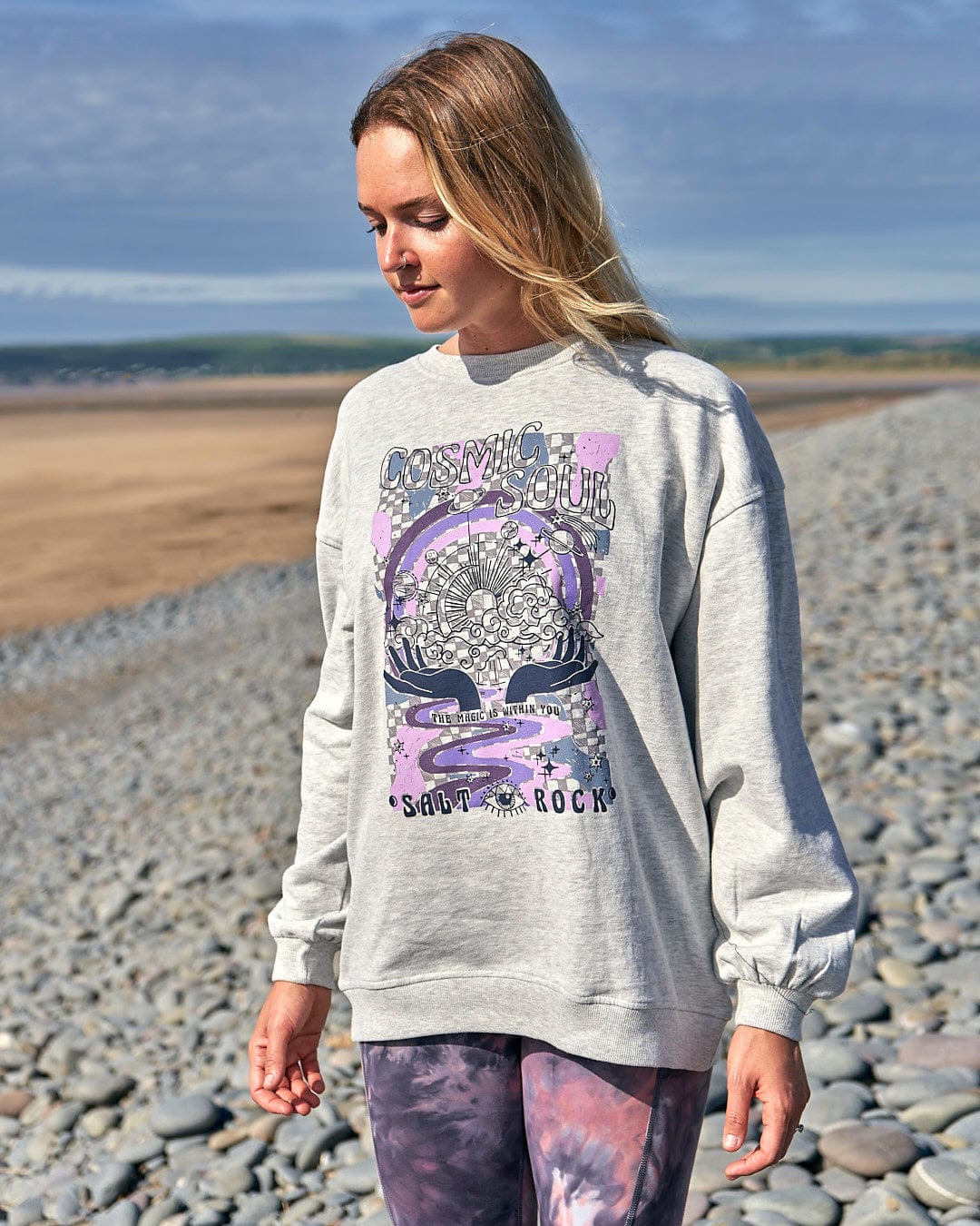 A woman in a Saltrock Cosmic Soul Womens Longline Sweat - Light Grey and leggings enjoying the beach.