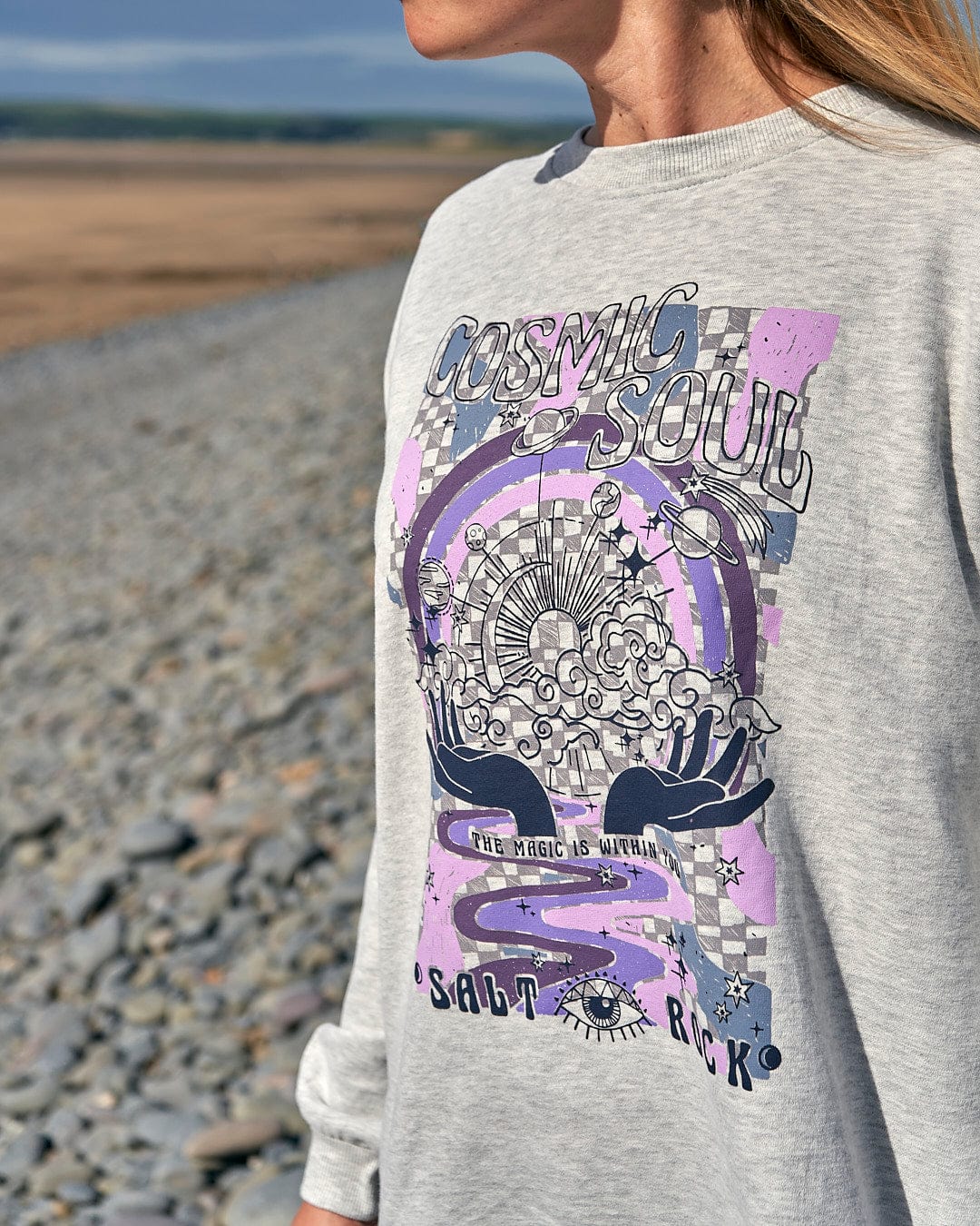 A woman wearing a Cosmic Soul - Womens Longline Sweat - Light Grey by Saltrock with comfort and style on the beach.