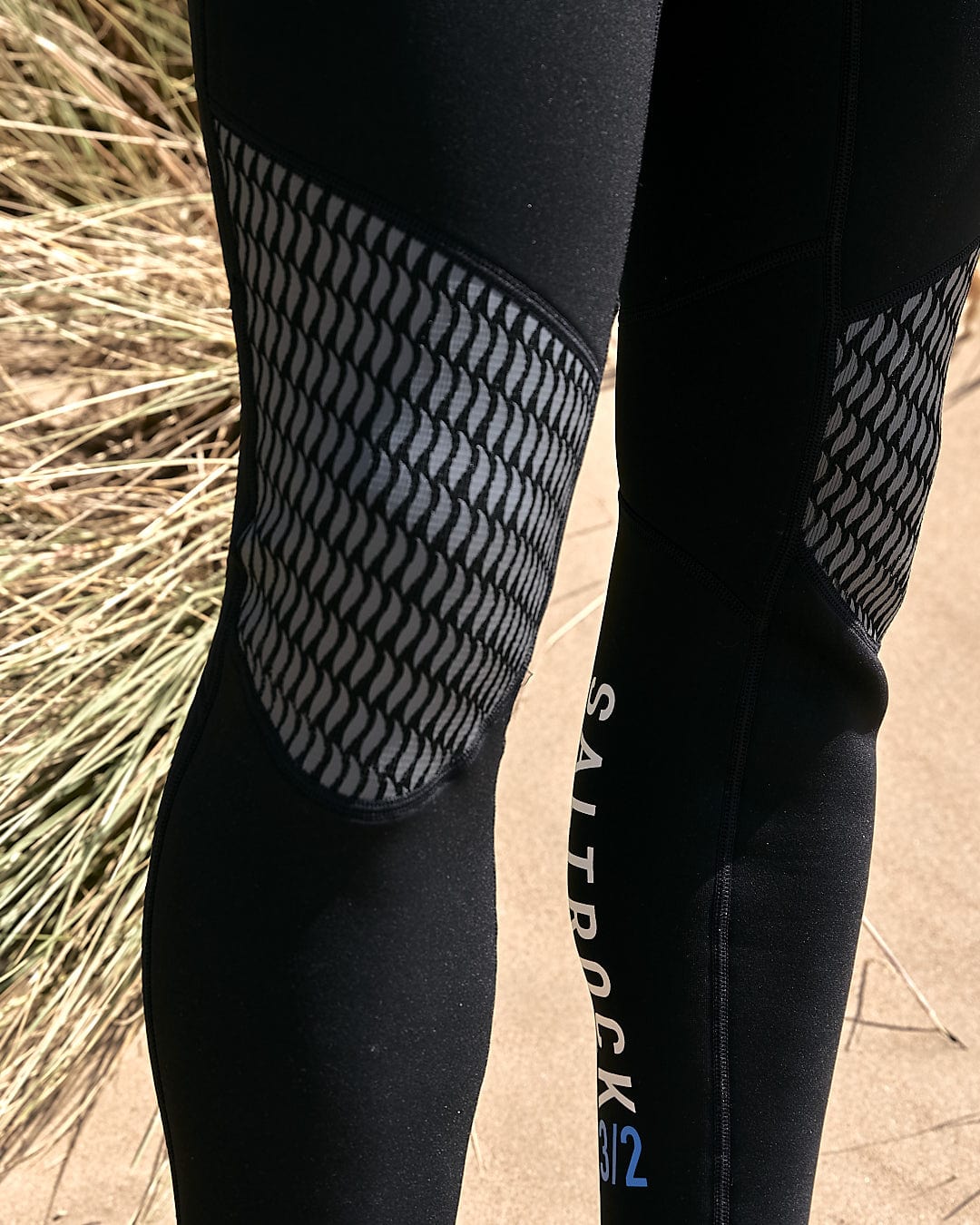 A man wearing Saltrock Core - Mens 3/2 Full Wetsuit - Blue/Black leggings standing in the sand.