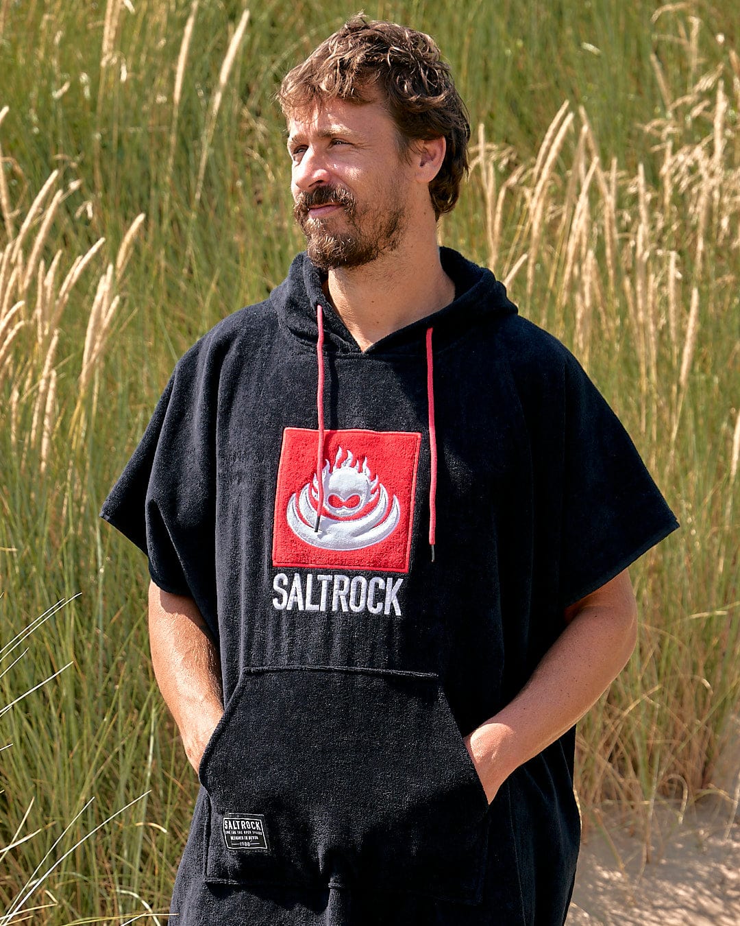 Man in a cotton towelling, absorbent Saltrock Corp Changing Towel - Black hoodie standing in a grassy field.