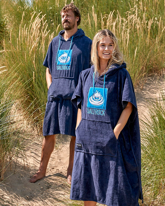 A man and woman standing in the sand wearing a Saltrock Corp - Changing Towel - Blue.