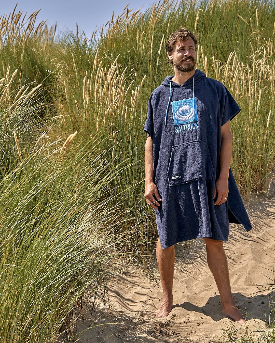 A man standing in the sand with a Saltrock Corp - Changing Towel - Blue.