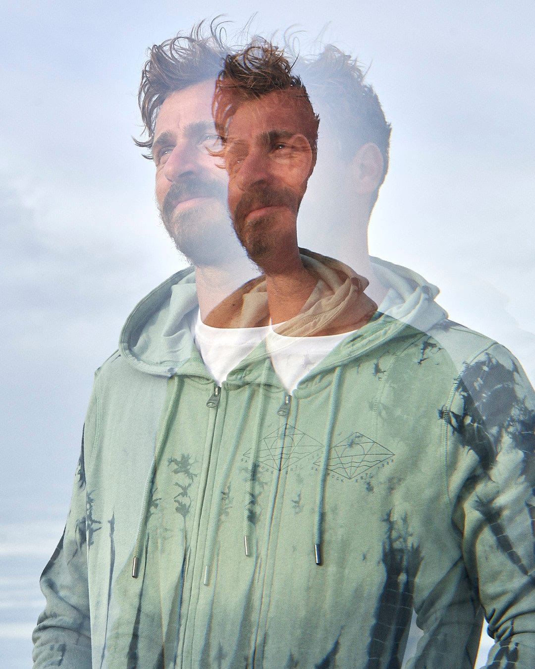 A man wearing a Saltrock Dimensions - Mens Zip Tie Dye Hoodie - Green hoodie with a surfboard.