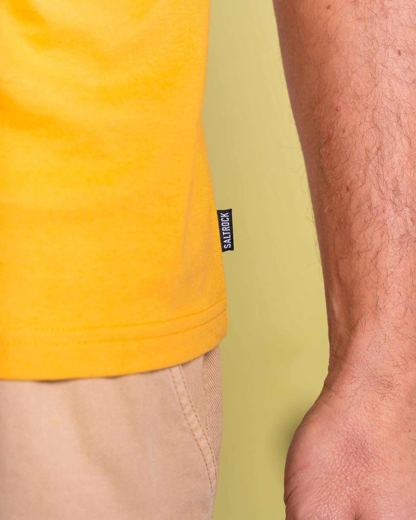 A person is seen wearing Saltrock's "Retro Camper" yellow T-shirt beside a matching camper, with a small black and white label on the shirt symbolizing adventure.