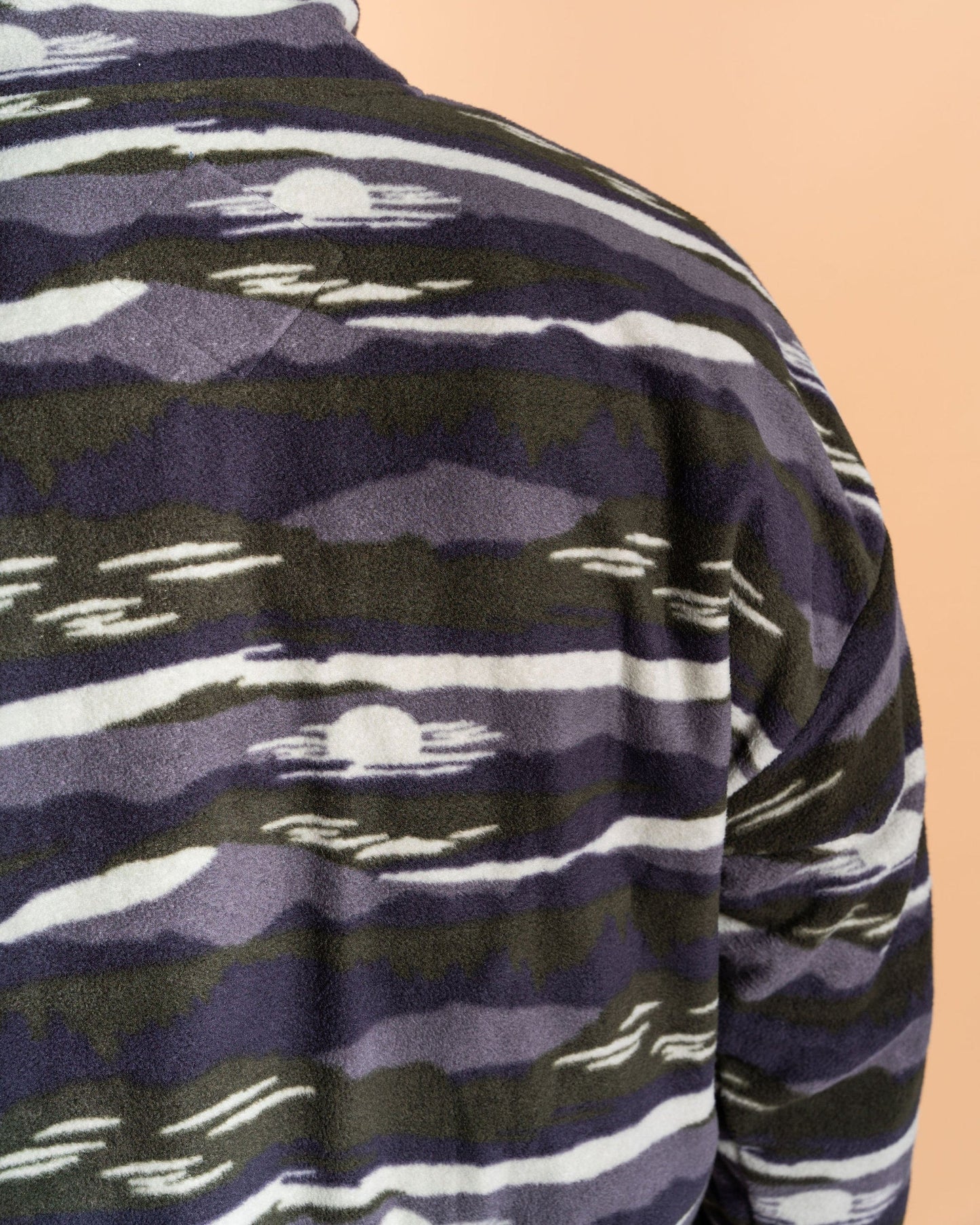 Close-up of a person wearing Saltrock's Hawker - Men's 1/4 Oversized Fleece in a green geometric pattern with stripes and circular shapes.
