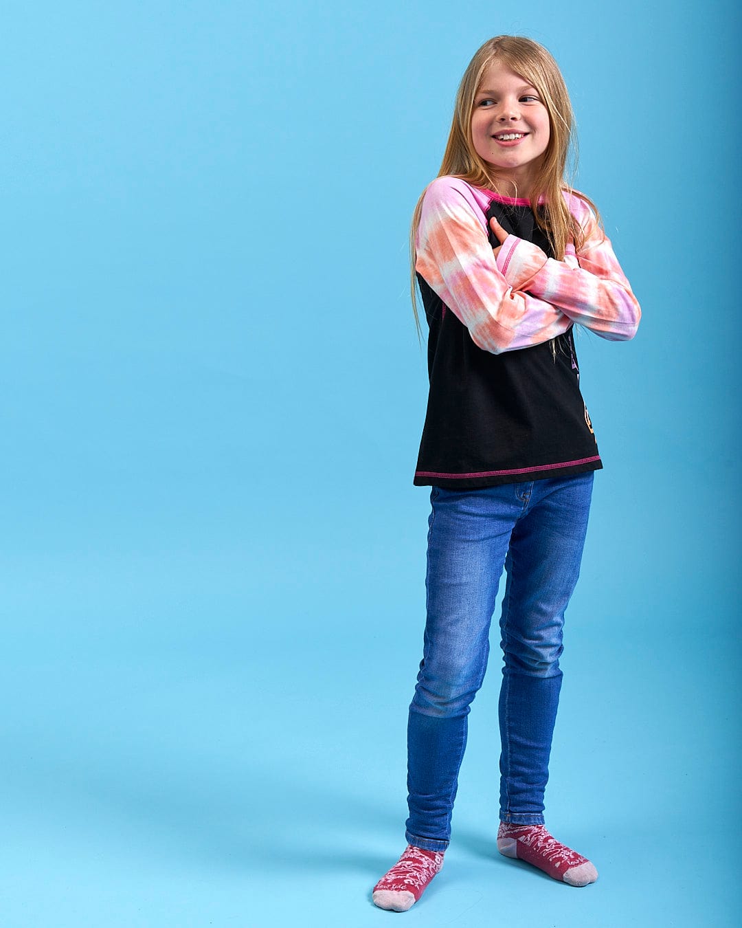 A little girl is standing in front of a Saltrock Elektra Tex - Kids Tie Dye Long Sleeve T-Shirt - Black background.