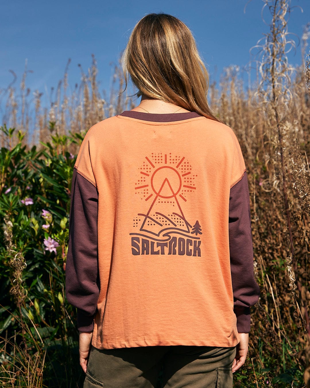 A woman is standing in a field wearing a comfortable Saltrock - Elissa Womens Boxy Sweat - Orange sweatshirt.