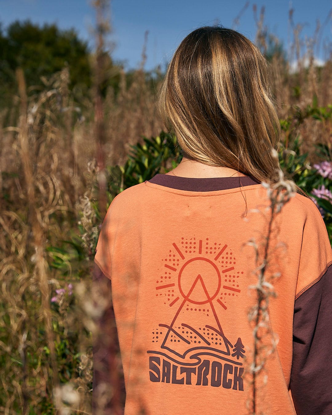 A woman wearing a comfortable Saltrock Elissa - Womens Boxy Sweat - Orange in a field.