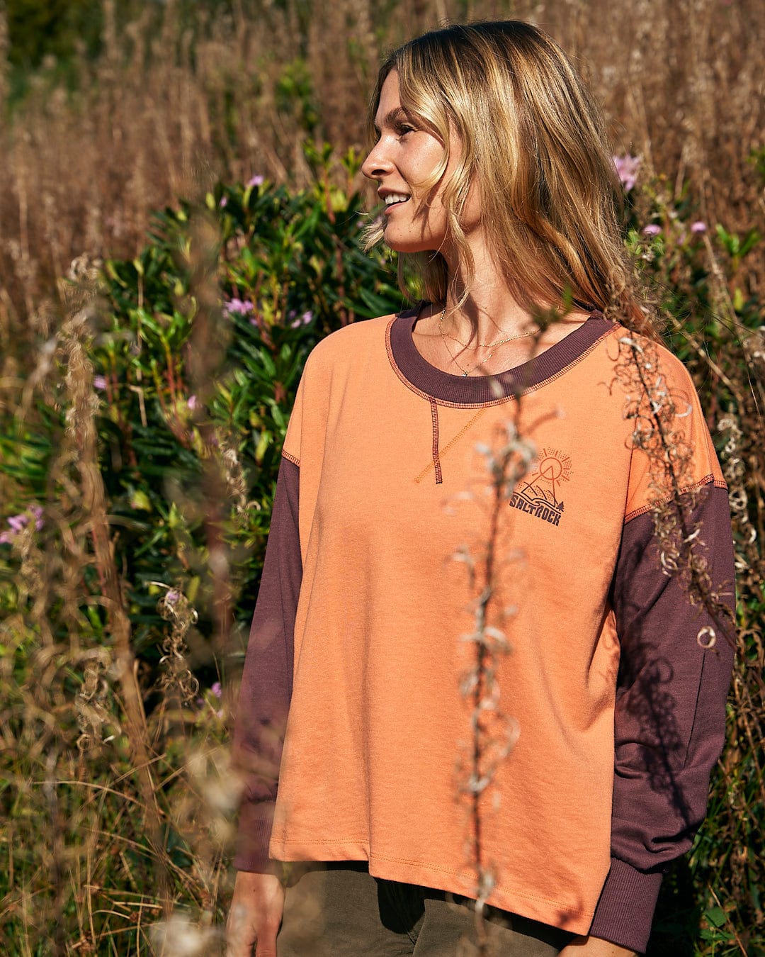 A woman in an Elissa - Womens Boxy Sweat - Orange shirt enjoying the comfort of a field. (Saltrock)